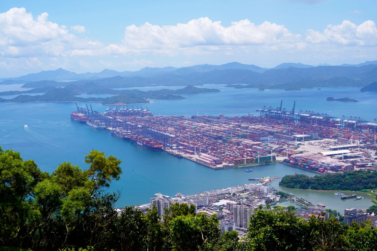 Aerial image of a bustling industrial port with containers in a scenic coastal setting.